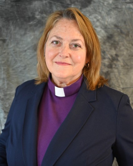 A professional photo of Bishop Escobedo-Frank wearing a black suit jacket with a purple blouse underneath and a white collar demonstrating Bishop status.